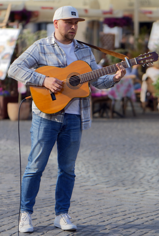 Talented street musician engrossed in playing his guitar on the cobblestone street